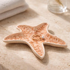 Grande coupelle étoile de mer en grès blanc avec émail rose poudré pyrité,  façonnée à la main par Terresme mise en situation dans une salle de bain avec des bijoux.