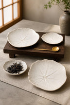 Set de quatre coupelles feuille de capucine en grès blanc, fait main par Terresme mise en scène sur tablette en bois foncé avec feuilles de thé et cuillère dorée.